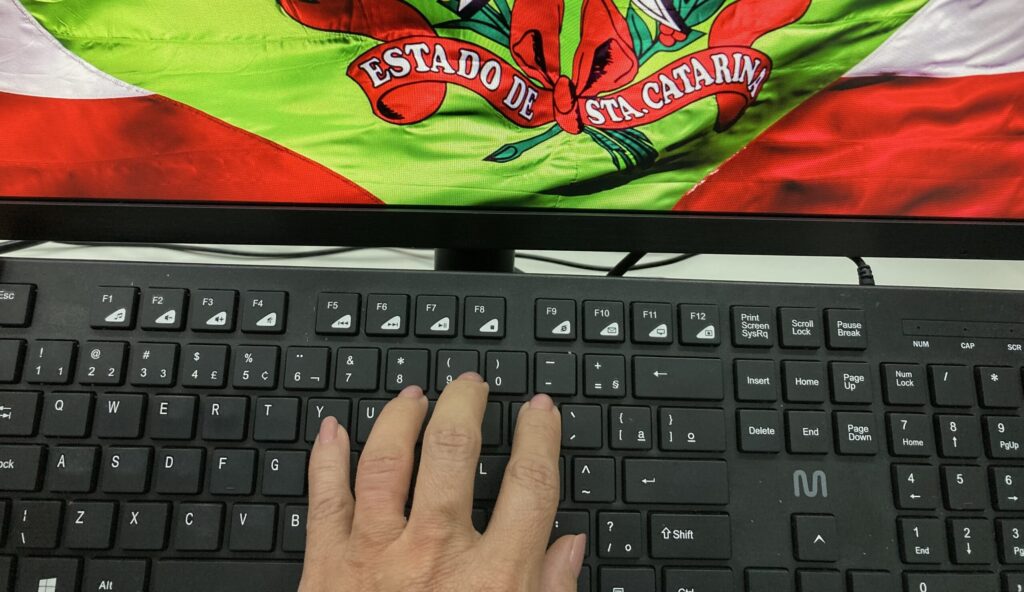 Mão digita ao teclado, com bandeira SC na tela